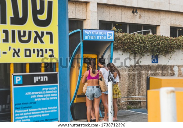 Tel\
Aviv/Israel-13/10/18: young women paying for parking, using ticket\
machine on a car parking in Tel Aviv. A ticket machine is a vending\
machine that produces paper or electronic\
tickets