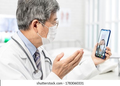 Tele medicine concept -  asian senior male doctor with face mask explain to the patient about the disease by video chat on cell phone in hospital - Shutterstock ID 1783060331