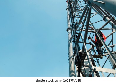 Telecom Worker Climbing Antenna Tower With Tools And Safety Equipment.