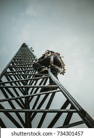 Telecom Worker Climbing Antenna Tower With Tools And Harness