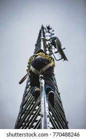 Telecom Worker Climbing Antenna Tower With Tools And Harness