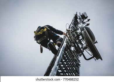 Telecom Worker Climbing Antenna Tower with Tools and Harness