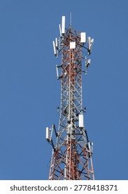 Telecommunications Cell Tower With Multiple Panel Antennas On Red And Silver Lattice Mast Against Clear Blue Sky