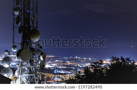 Telecommunications tower, antenna and satellite dish and city at night as background