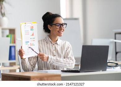 Telecommuting Concept. Happy Female Manager Having Video Call On Laptop, Giving Virtual Presentation And Smiling. Woman Showing Document Paper With Graphs And Diagrams To Webcam