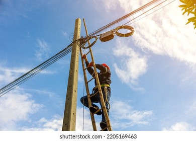 A telecoms worker is shown working from a utility pole ladder while wearing high visibility personal safety clothing, PPE, and a hard hat.	