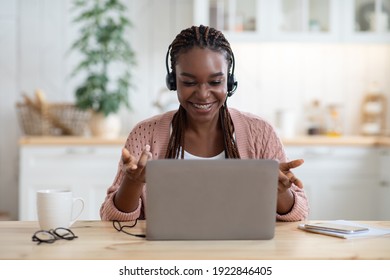 Teleconference. Positive Black Woman In Headset Having Video Call On Laptop In Kitchen, Talking And Gesturing At Computer Web Camera, Enjoying Online Conversation And Distant Communication, Free Space