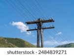 Telegraph pole. Wires of overhead telephone and telegraph communication lines on a wooden pole in a mountainous area. Telecommunications landscape against the backdrop of green mountains and blue sky.