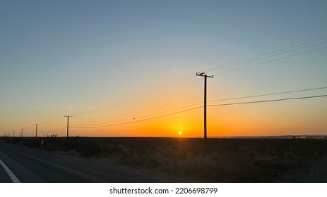 Telegraph Poles And Wires At The Side Of A Desert Highway In California, Silhouetted At Sunset