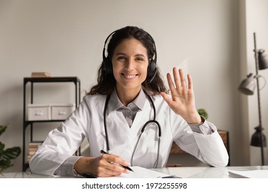 Telehealth. Headshot Portrait Of Smiling Latin Woman Doctor Physician Wear Headphones Look At Camera Wave Hand To Spectators. Young Female Medic Consult Remotely At Virtual Online Meeting With Patient