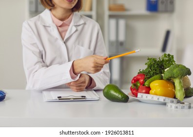 Telehealth and online nutritiologist concept. Woman doctor nutritiologist sitting and pointing at fresh vegan healthy ingredients to patient online during videocall or distant meeting - Shutterstock ID 1926013811