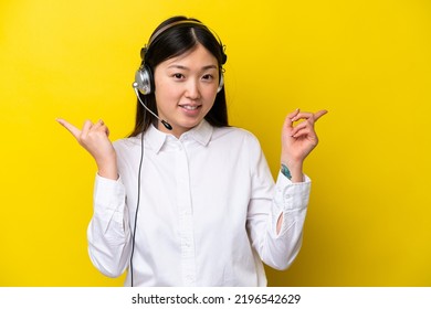 Telemarketer Chinese Woman Working With A Headset Isolated On Yellow Background Pointing Finger To The Laterals And Happy