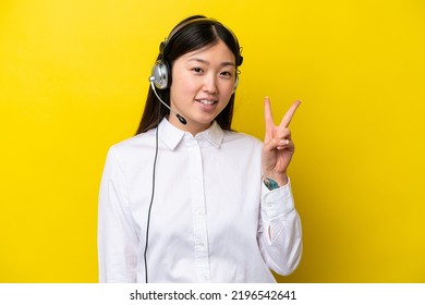 Telemarketer Chinese Woman Working With A Headset Isolated On Yellow Background Smiling And Showing Victory Sign