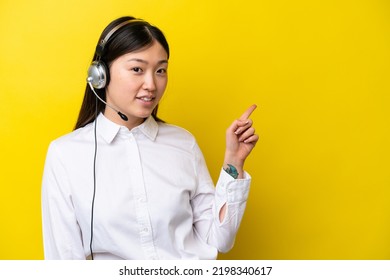 Telemarketer Chinese Woman Working With A Headset Isolated On Yellow Background Pointing Finger To The Side