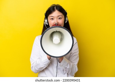 Telemarketer Chinese Woman Working With A Headset Isolated On Yellow Background Shouting Through A Megaphone