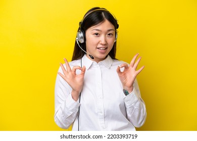 Telemarketer Chinese Woman Working With A Headset Isolated On Yellow Background Showing An Ok Sign With Fingers