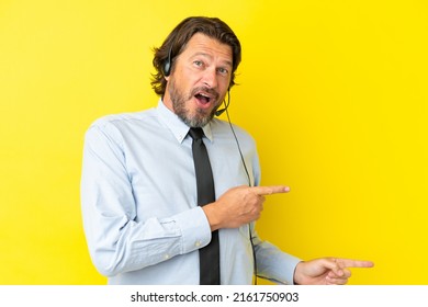 Telemarketer dutch man working with a headset isolated on yellow background surprised and pointing side