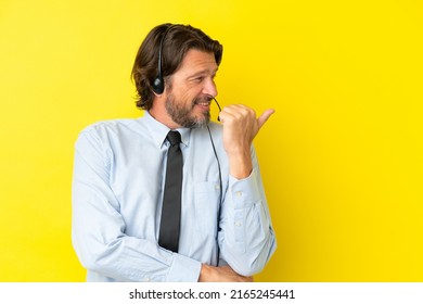 Telemarketer dutch man working with a headset isolated on yellow background pointing to the side to present a product