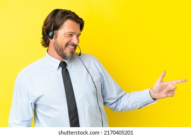Telemarketer dutch man working with a headset isolated on yellow background pointing finger to the side and presenting a product