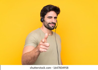 Telemarketer man working with a headset over isolated yellow background points finger at you