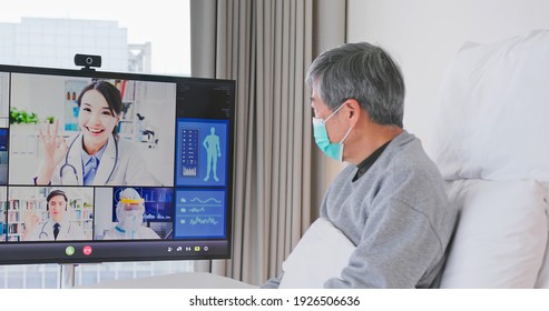 Telemedicine concept - asian senior man patient lying on bed has video call with doctor team by big screen TV in a hospital ward or at home