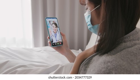 Telemedicine Concept - Asian Woman Patient Wearing Face Mask Is Talking About Her Sick Symptom To Female Doctor By Mobile Phone On Bed