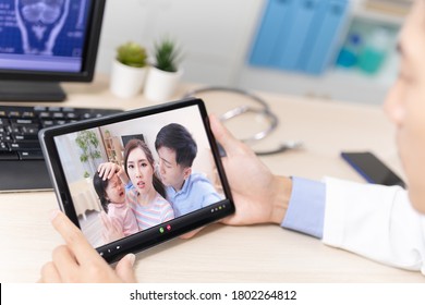Telemedicine concept - back view of asian male pediatrician is listening to the family on digital tablet