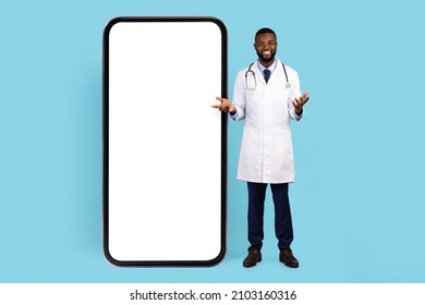 Telemedicine Concept. Black Doctor Standing Near Big Blank Smartphone With White Screen, African American Male Therapist Advertising Medical App, Posing Isolated On Blue Background, Mockup, Collage