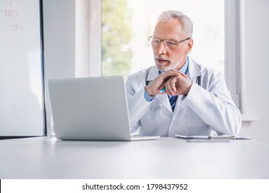 Telemedicine Concept. Senior Doctor Talking With Patient Using Laptop Online Video Webinar Consultation While Sitting In Clinic Office.