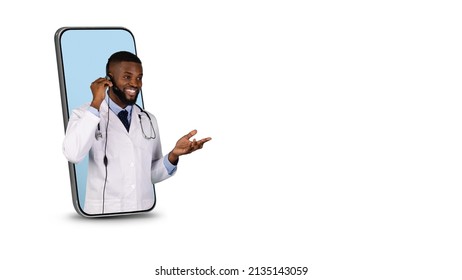 Telemedicine. Friendly Black Doctor Wearing Headset Peeking Out Of Big Smartphone Screen Over White Background, Professional Therapist Consulting Patient Online, Creative Collage With Copy Space