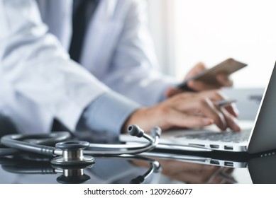 Telemedicine, Medical Research, Technology And Internet Concept. Doctor Using Mobile Smart Phone, Working On Laptop Computer With Stethoscope On Desk, Close Up