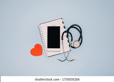 Telemedicine Or Telehealth Virtual Visit, Video Visit, Remote Doctor Video Chat Consultation Concept With Smartphone, Open Notepad And Stethoscope On Blue Background