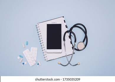 Telemedicine Or Telehealth Virtual Visit, Video Visit, Remote Doctor Video Chat Consultation Concept With Smartphone, Open Notepad And Stethoscope On Blue Background