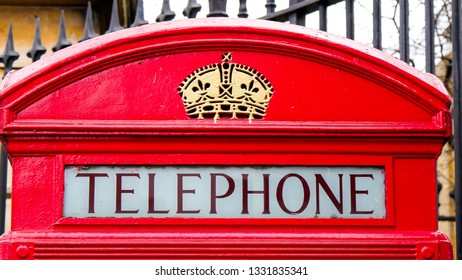 The telephone booth on the front of a black gate. With a royal crown carved on top it is one of the many red telephone booths in London - Shutterstock ID 1331835341