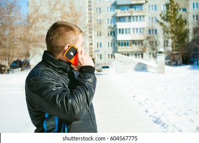 Telephone calls men. The guy is talking on cell phone street in winter,dressed  warm clothes, holds his hand phone at ear, bright orange sheath case, emotionally smiling