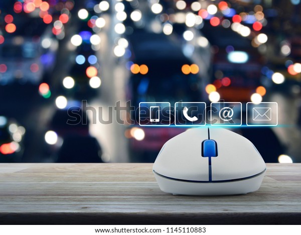 Telephone, mobile phone, at and\
email buttons with wireless computer mouse on wooden table over\
blur colorful night light city with cars, Customer support\
concept