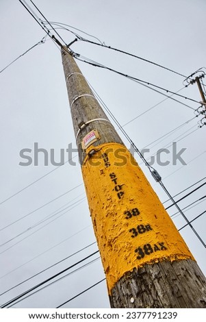 Telephone pole with yellow patch of paint and view of wires crisscrossing over overcast sky