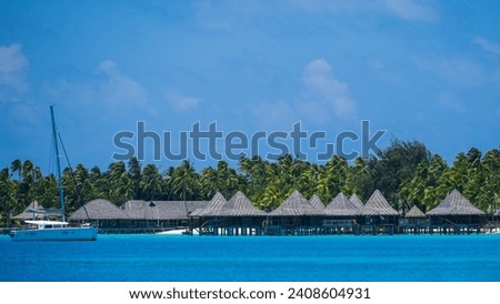 A telephoto  200mm shot of thatched roof huts built over the water in French Polynesia.
