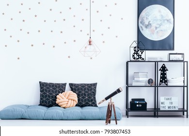 Telescope Next To Blue Mattress With Cushions In Kid's Bedroom Interior With Stars Stickers And Moon Poster On White Wall Above Shelves