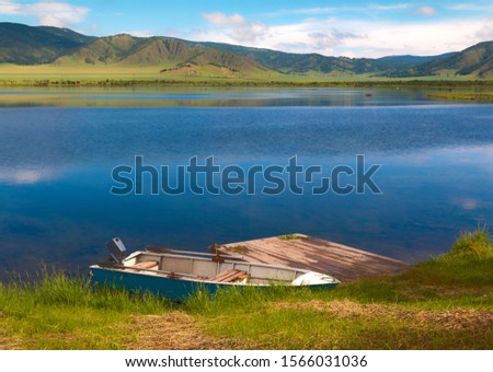 Teletskoye Lake, Altai Republic, Southern Siberia, Russia. Panoramic view of famous Lake Teletskoye  with fishing boat surrounded by the majestic mountain range of Altay against a clear blue sky