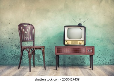 Television set receiver from 50s on wooden outdated analog TV stand and old classic chair front color textured aged concrete wall background. Vintage style filtered photo - Shutterstock ID 2060419439