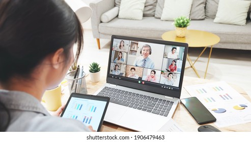 telework concept - rear view of asian woman using laptop to join a video meeting and hold digital tablet at home