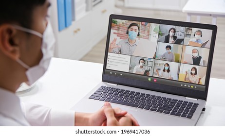 telework concept - rear view of asian businessman wearing face mask is having a group video meeting by laptop in the office - Powered by Shutterstock