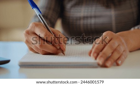 Teleworker at desk transcribing data from laptop to notepad, finalizing project. Remote worker solving job tasks before deadline, writing info on paper using pen, camera B close up shot