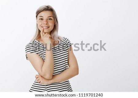 Tell me more I am interested. Portrait of charming young woman with braces on teeth, smiling broadly, leaning face on fist and smiling broadly, being intrigued and involved in conversation