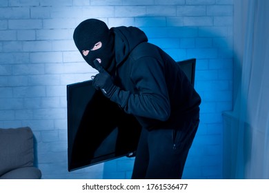 Tell No One. Sneaky Criminal Wearing Black Balaclava Hat Stealing Television Or Computer Monitor