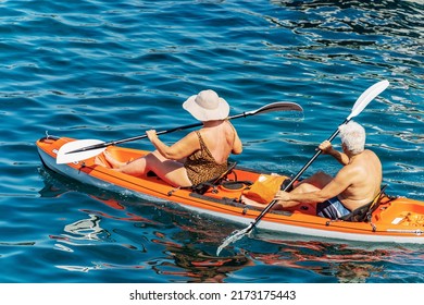 TELLARO, ITALY - July 21, 2019: A Mature Couple Aboard An Orange Kayak, Paddling In The Blue Mediterranean Sea, On A Sunny Summer Day. Gulf Of La Spezia, Liguria, Italy, Europe.