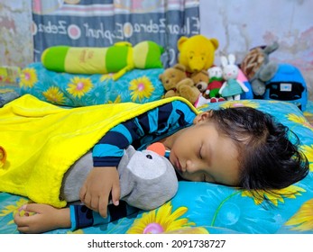 Temanggung, Indonesia - December 12, 2021 : Cute little girl sleeping with a stuffed penguin and blanket on the bed.
