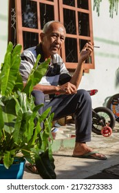 Temanggung, Indonesia - June 29, 2022 : Old Man Sitting On The Porch Smoking