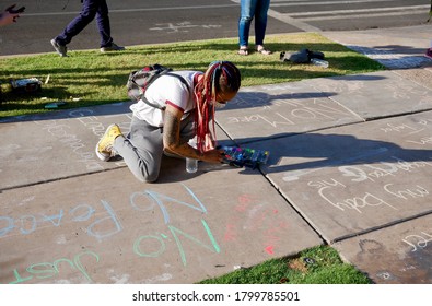 TEMPE, AZ/USA - JULY 2nd, 2020: Unidentified Woman W/ Colorful Braids, Face Mask & Variety Of Chalk Markers Crouches Down To Write A Chalk Message In Support Of BLM, Outside Of Tempe City Hall.